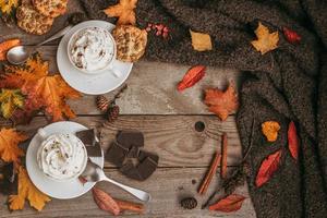 otoño, hojas de otoño, taza de café humeante caliente y una cálida bufanda sobre fondo de mesa de madera. foto