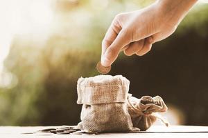 hand puting coins in money bag for saving on table background photo