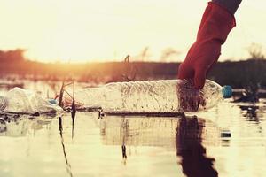 woman hand picking up garbage plastic for cleaning at river with sunset photo