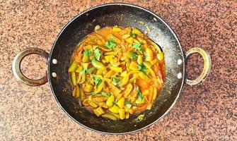 Parwal curry - Pointed gourd curry - in black wok on brown background photo