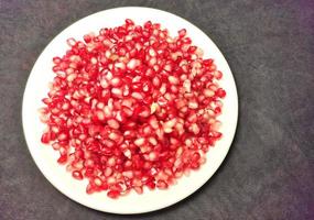 Pomegranate seeds placed on a white plate on a dark background photo