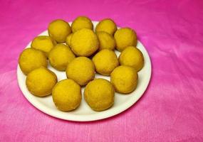 festival indio dulce - besan laddu, hecho con harina de gramo, azúcar y ghee, colocado en un plato blanco sobre un fondo de color. foto