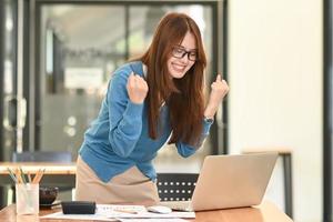 Young woman showing joy in office, businesswoman raising hands in smiling face, stock market, business concept. photo