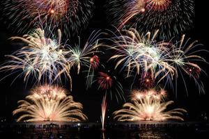 Festive fireworks display light up over night sky at the beach. Colorful firework celebration on dark background. photo