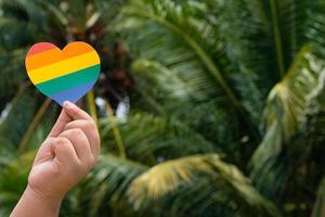 mano sosteniendo papel de color arco iris cortado en forma de corazón, concepto para lgbtq foto