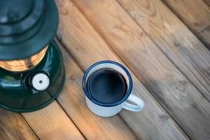 Selective focus white enamel coffee mug and coffee set in the garden with ancient lanterns in a camping atmosphere. soft focus. photo