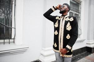 hombre africano mega elegante en pose de chaqueta tradicional. chico negro de moda con sombrero y gafas de sol con cigarro en la mano. foto