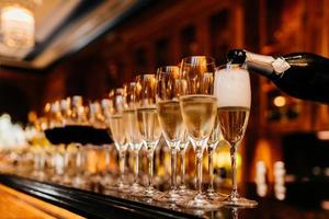 Row of glasses filled with champagne and other beverages, someone holds bottle and fills in glasses. Bar counter. Banquet photo