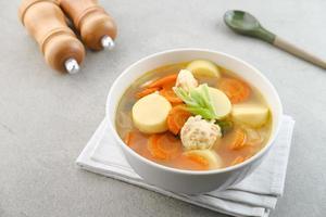 Clear soup with egg tofu, carrot and shrimp meatballs. Served in white bowl on grey background. photo