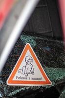 Warning sign of children inside a car after an accident with bloody broken glass. Translation Child in the car. Close-up of white baby on board sticker on car back window. Vertical photo. photo