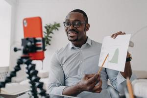 African american business analyst shows economic graph to coworkers online by video call with phone photo