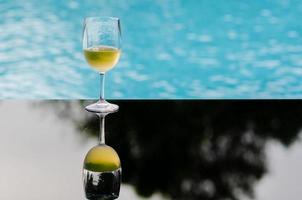 A glass of white wine puts on table at swimming pool for Holiday and summer drink concept. photo