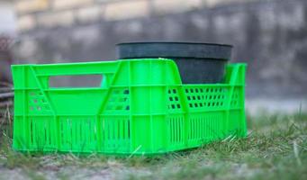 Plastic empty green box in the garden for plants or harvesting. On a sunny day in early spring. Gardening concept. Household crop collection and storage box standing in the backyard. photo