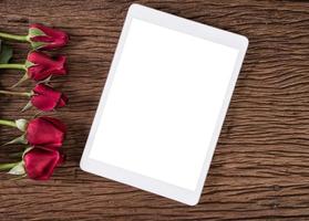 Tablet computer and red rose on old wooden background photo