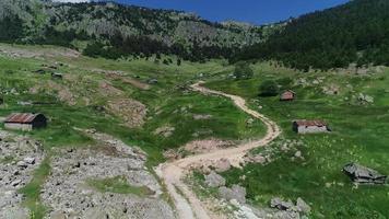 plateau verdoyant et maisons. maisons des hautes terres dans la vallée verdoyante entre les montagnes, l'herbe se balançant du vent. il y a un chemin de terre. video