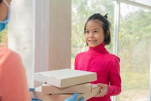 servicio de entrega en camiseta, con máscara protectora y guantes dando orden de comida, sosteniendo tres cajas de pizza en el frente de la casa, mujer aceptando la entrega de cajas del repartidor durante el brote de covid-19. foto