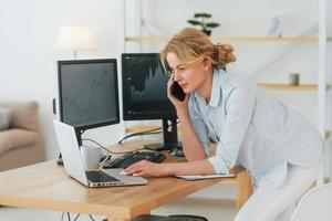 Standing and using laptop. Female stock broker in formal wear is working in the office photo