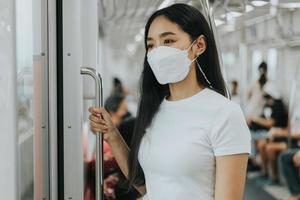 mujer asiática con máscara protectora de pie y esperando el tren del cielo. mujer con máscara protectora quirúrgica en un transporte público. nuevo concepto normal. foto