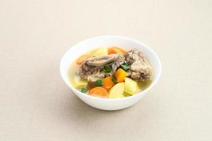 Sop Iga, Beef ribs soup, is Indonesian soup. Made from ribs, carrots, leeks, and potatoes. Served in white bowl. Selected focus photo