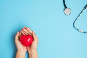 médico mano sosteniendo forma de corazón rojo con estetoscopio sobre fondo azul. cuidado de la salud, seguro de vida y concepto del día mundial del corazón foto