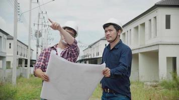 Two Asain confident engineers discussing blueprint while standing at construction site video