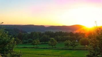 puesta de sol en el sarre en un prado con árboles y vistas al valle foto