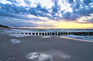 puesta de sol en la playa del mar báltico. reflejo en la playa. los espigones llegan al mar. foto