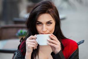 Young stylish woman drinking coffee in a city street.Stylish hipster girl drinking coffee in street. Outdoors fashion portrait of young beautiful girl drinking coffee. photo