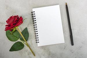 Note book with red roses and pen on marble desk. Top view. Flat lay. Copy space. photo