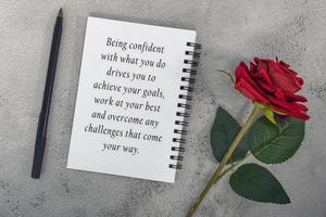 cita motivacional en un cuaderno con rosas rojas y un bolígrafo. foto