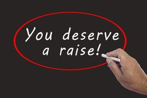 Male hand writes in white chalk pencil the word YOU DESERVE A RAISE. photo