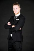 Portrait of young smart and handsome business man in black suit standing on isolated black background. photo