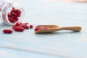 medicinas rojas en las botellas de vidrio sobre la cuchara de madera y la mesa azul. medicina farmacéutica o píldoras, tabletas y cápsulas de vitaminas foto