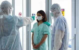 COVID-19, Corona Virus outbreak quarantine and epidemic spread concept. Asian doctors wear PPE  glove and face mask checking patient temperature at quarantine room in hospital photo