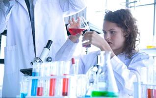 Young woman and man reserchers, scientists, technicians or students conducting research or experiment by using scientific, medical equipment or device in chemistry laboratory photo