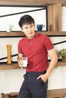 Smart, young and healthy Asian man with casual  red t-shirt having breakfast with milk in the loft style kitchen room photo