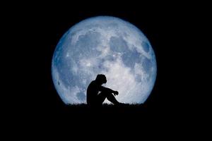 Desperate and lonely man in the background of the moon at night. Desperate, heartbreaking, and lonely concepts photo