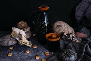 Old dog skull, jug and stones on witch table. Enchanted drink with flower petals photo