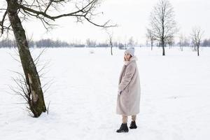 Young girl in beige clothes, fur coat made of artificial fur walks in winter photo