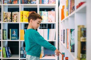 un niño alcanza un estante de libros para niños en la librería. foto