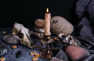 viejo cráneo de perro, velas encendidas, runas de madera y piedras en la mesa de brujas. foto