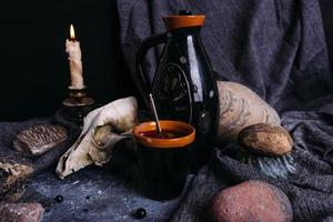 Old dog skull, jug and stones on witch table. Enchanted drink with flower petals photo
