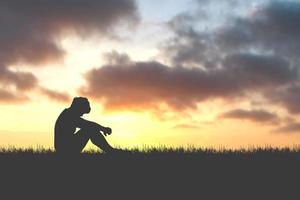 The concept of despair, discouragement, and loneliness. Silhouettes of people sitting with their heads down in sorrow in the meadows. photo