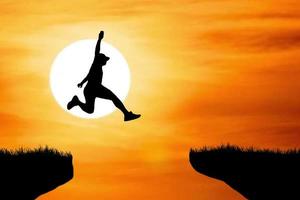 Silhouette of an athlete jumping on a rocky cliff photo