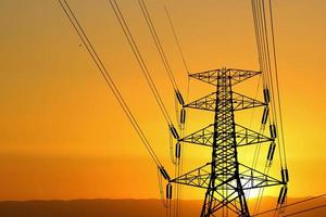 Silhouette of high voltage poles with electric wires. Silhouette of high voltage power line cables in an orange evening sunset. Steel structure of electric poles. electric power transmission concept photo