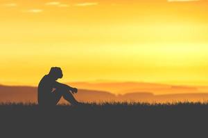 The concept of despair, discouragement, and loneliness. Silhouettes of people sitting with their heads down in sorrow in the meadows. photo