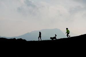 dos mujeres corren en las montañas con un perro foto