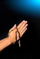 Praying Hands holding rosary beads on black background photo