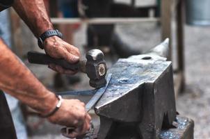 un herrero artesano golpea con un martillo sobre el hierro para dar forma foto