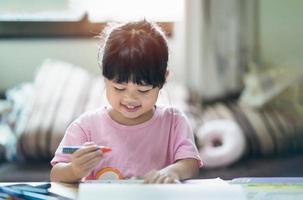 lindo niño pequeño pintando con pinturas de colores. chica asiática usando crayón dibujo color.bebé artista actividad estilo de vida concepto. foto